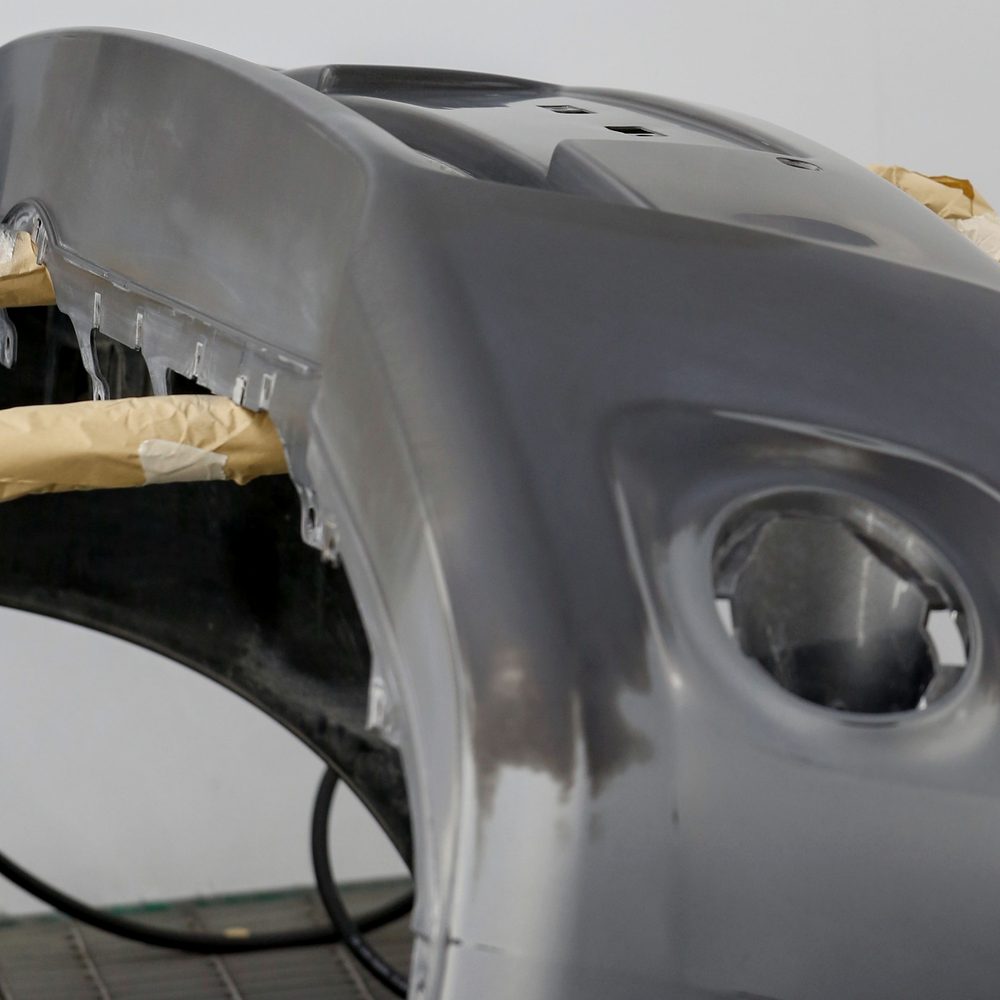 Licensed stock photograph: a bumper cover in grey primer resting on masking paper inside a spray booth.