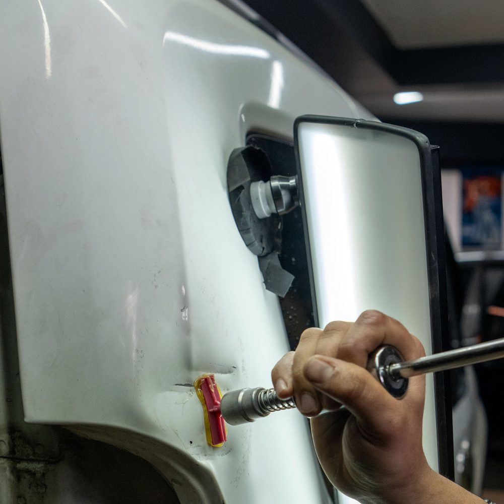 Licensed stock photograph: a hand working a dent puller against a white panel, with a lit reflection board held beside it.