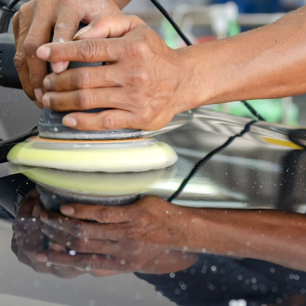 Licensed stock photograph: two hands running a polisher across a car hood, the pad reflected in the paint.