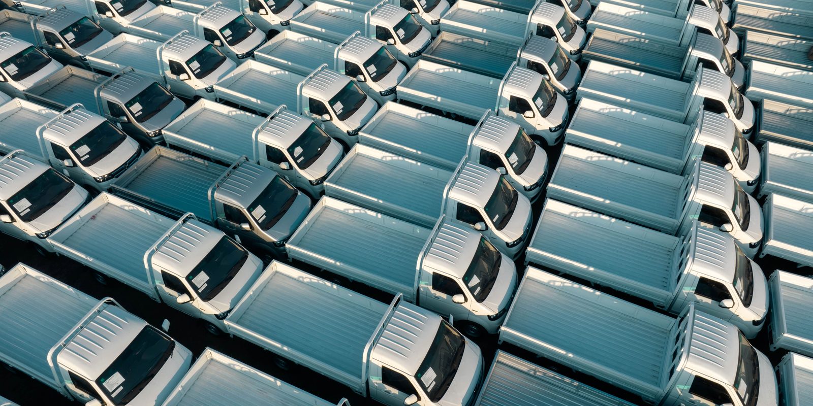 Licensed stock photograph: rows of white flatbed work trucks parked in a yard, seen from above.